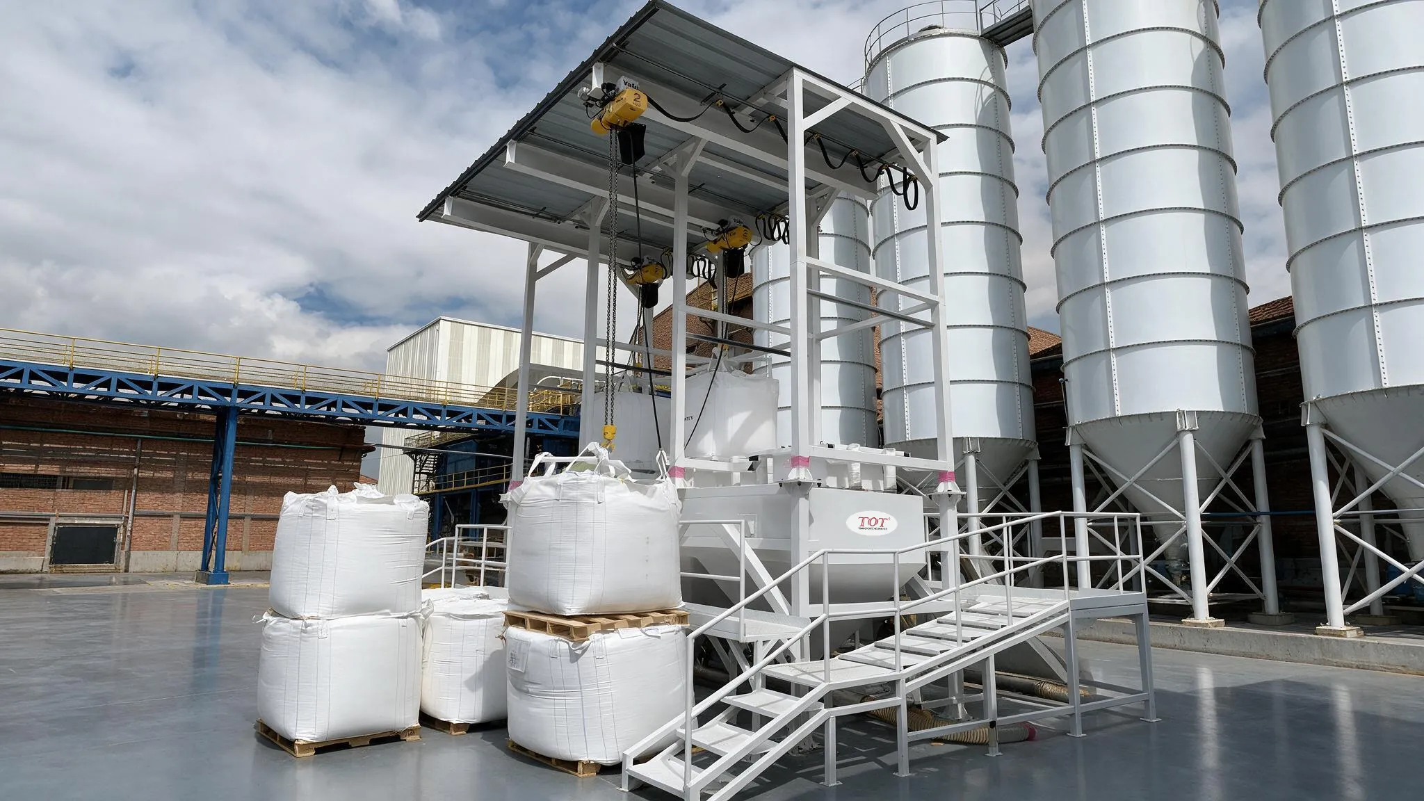 Estación doble de descarga de Big Bag con techo y polipastos operando a la intemperie, alimentando una batería de silos mediante transporte neumático.