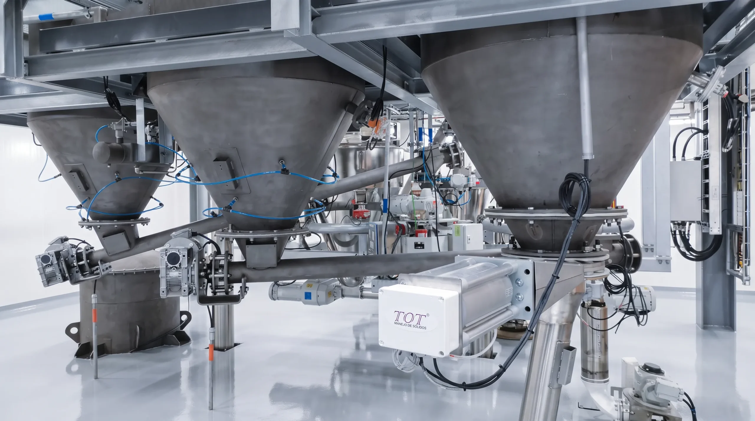 Batería de tolvas de acero inoxidable con tornillos dosificadores y sistema de fluidización, alimentando una línea central de transporte neumático.